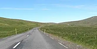 A paved road running between green fields with hills rising on either side