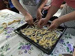 Two women folding long pieces of dough on a tray into various shapes