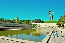 Monument depicting a woman with a sword in the background, a pond with a Cyrillic inscription at the side in front
