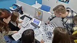 A group of people gathered around a desk, holding printouts with Hutsul ornaments