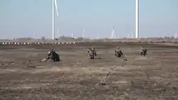 Russian servicemen demining an area in front of wind power plants and next to dragon teeth.