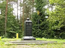 A stone pillar with the inscription about the site. Trees behind.
