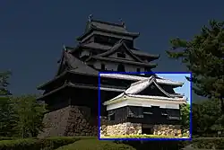 Small tower attached to a castle with dark walls, dark roofs on a platform of unhewn stones.