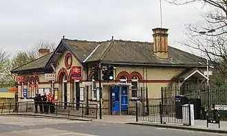 A yellow brick building with a ramp in front photographed from across the street. On the side of a building there is a sign with a double arrow logo on it.