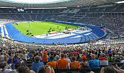 Photo of the Olympic Stadium with a blue athletics track around green grass, seen from the spectator area