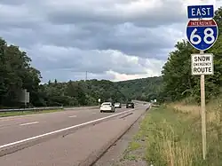 A four-lane freeway in a forested area with a sign saying East I-68. Snow Emergency Route.