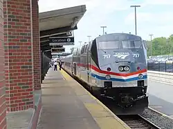 A gray diesel locomotive with red, white, and blue stripes of equal width on the side. The stripes narrow and angle downwards on the front under the black-painted cab area.