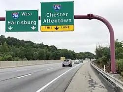 Three lanes of a six-lane highway, with two signs
