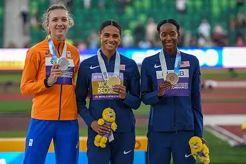 Photo of three standing women seen from the waist up wearing tracksuits and with medals around their necks