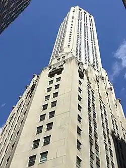 One of the corners as seen from street level. The lower section of the building has a flat chamfered corner connecting two sides that meet at an acute angle. The upper section consists of a square tower.
