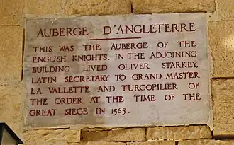 A plaque with the inscription AUBERGE D'ANGLETERRE: THIS WAS THE AUBERGE OF THE ENGLISH KNIGHTS. IN THE ADJOINING BUILDING LIVED OLIVER STARKEY LATIN SECRETARY TO GRAND MASTER VILETTE AND TURCOPILIER OF THE ORDER AT THE TIME OF THE GREAT SIEGE IN 1565