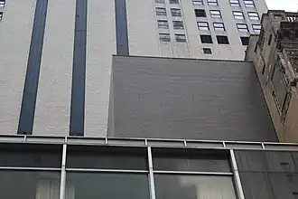 View of the penthouse, a black brick structure above the fourth story. The facade of another building can be seen behind the penthouse.