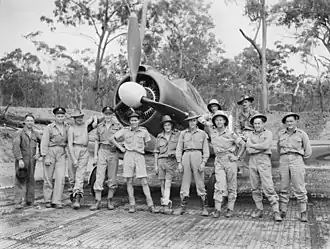 Twelve men wearing military uniforms standing in front of a single-engined World War II-era propeller fighter aircraft