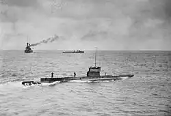 A submarine moves across the surface of the ocean, and two warships can be seen in the background.