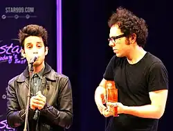 A Great Big World performing. A member of them is playing the guitar, while the other is singing to a microphone