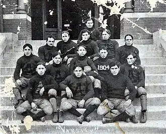 Black & white image illustrating 14 American football players in their uniforms with a single "A" visible on most jerseys and "1904" visible on one