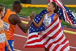 Photo of a male athlete and a female athlete with an American flag giving each other a handshake