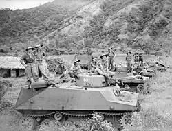 Black and white photograph of men wearing military uniforms standing on top of tanks parked on a grassed area