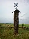 A roofed pole tipped with an ornate iron cross with floral motif. Angiras village, northwest of Josvainiai.