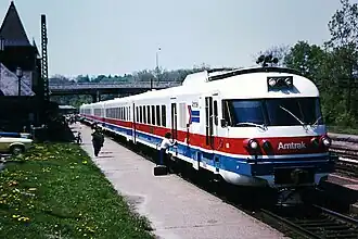 A white passenger trainset with red and blue horizontal stripes on the side