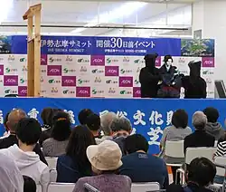 Two black clothed and masked people operating a large doll on stage.