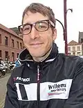 A man wearing a cycling windbreaker smiling into the camera