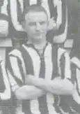 A white man with his arms folded, wearing a striped sports shirt.