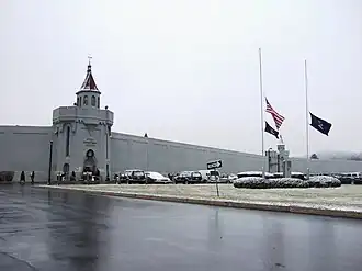 wall of building with text that says Attica Correctional Facility. Flags are visible outside at half-staff.