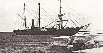 Three-masted ship with funnel to rear, anchored by the bow to an ice shelf