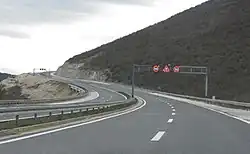 Variable traffic signs placed on a gantry indicating speed limit for each traffic lane and slippery road surface warning.