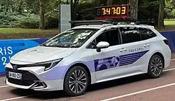 A car with the Olympics branding is on the side of a street, next to the a large timer.