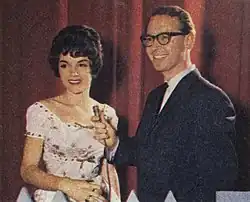 Brian Henderson stands next to Patsy Ann Noble holding a microphone towards her