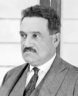 Black and white photo of a white man with a mustache, wearing a suit.