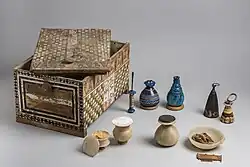 A painted wooden box with lid askew and its contents of stone and glass vessels neatly arranged beside it