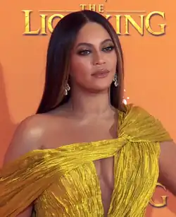 Beyoncé wearing a yellow dress with gradient dark and lighter brown hair in front of an orange wall