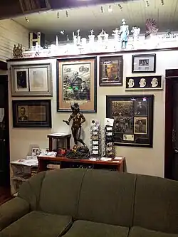 Photograph of the interior of a building; there are many framed photos on the wall as well as sculptures and other memorabilia