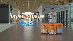 An image of Drew Arellano standing in a transport station, with three orange suitcases displaying his picture. The show title is displayed on the left center of the image. The text "Sa" is displayed below the title. The logo of GMA Network is displayed below the text "Sa".