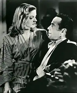 Lauren Bacall in black and white, sitting on Humphrey Bogart's lap facing right in the film To Have and Have Not in 1944