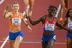 Photo of two female athletes holding up a baton, three other athletes are only partially visible