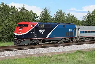 A blue diesel locomotive with an angular white stripe, red nose, and a red sill stripe pulling a train
