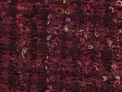 A dark pink fabric with a roughly-woven darker check pattern. It is covered in less densely-woven small loops in lighter shades of pink and yellow.