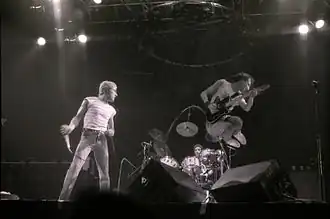 Roger Daltrey holding a microphone and Pete Townshend jumping on stage