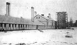 Long, light-colored barn with several towers and a silo with scaffolding