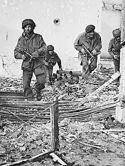 Four men in a bomb damaged building, with debris on the ground