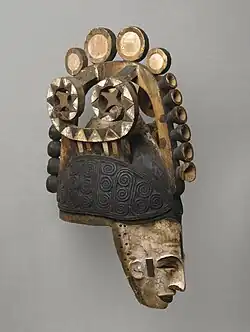 Igbo maiden spirit helmet mask (Agbogho Mmwo); early 20th century; 50.2 x 14.6 x 30.5 cm (193⁄4 x 53⁄4 x 12 in.); Brooklyn Museum. This helmet mask has long narrow face, painted white; narrow protruding sharp nose; slit eyes; open mouth showing teeth; small ears