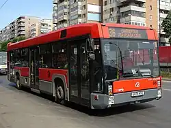A red and grey bus grinds to a halt on the street