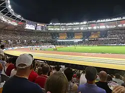 Photo of spectators in elevated seats around a red athletics track of which half is visible