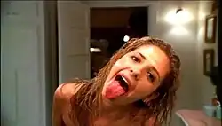 Sarah Michelle Gellar (as Faith-in-Buffy's-body) leaning in front of a bathroom mirror, hair wet from a bath and with a towel wrapped around her, sticking out her tongue with her head tilted to her left.