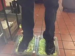 An anonymous employee standing on two open boxes of lettuce