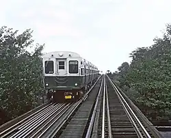 An unsaturated photograph of a train painted green on the bottom and white on the top, viewed head-on on the viewer's left track